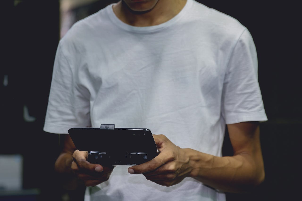 our-story-01 A young man in a white shirt using a smartphone game controller indoors.